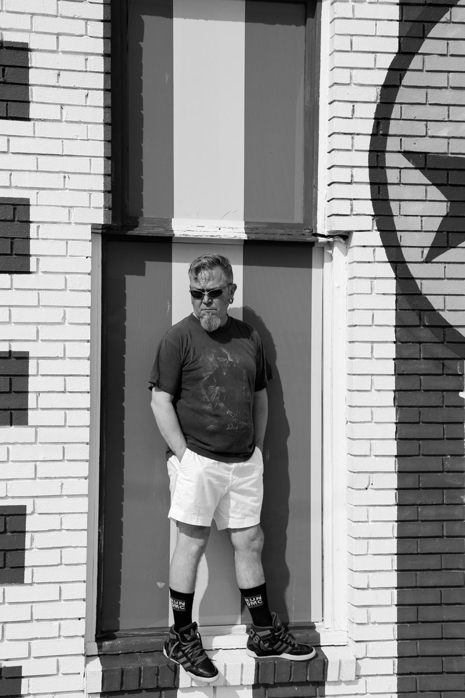 Mighty Rock standing in a painted window frame, wearing sunglasses and Run-DMC socks
